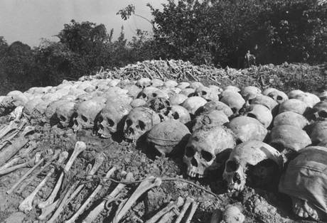 A black and white photograph showing rows of human skulls and bones laid out on the ground in an outdoor setting, likely a memorial or mass grave site from the Cambodian genocide.