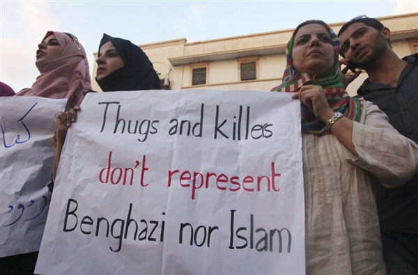 A photograph of protesters in Benghazi holding a sign that reads 'Thugs and killers don't represent Benghazi nor Islam'.