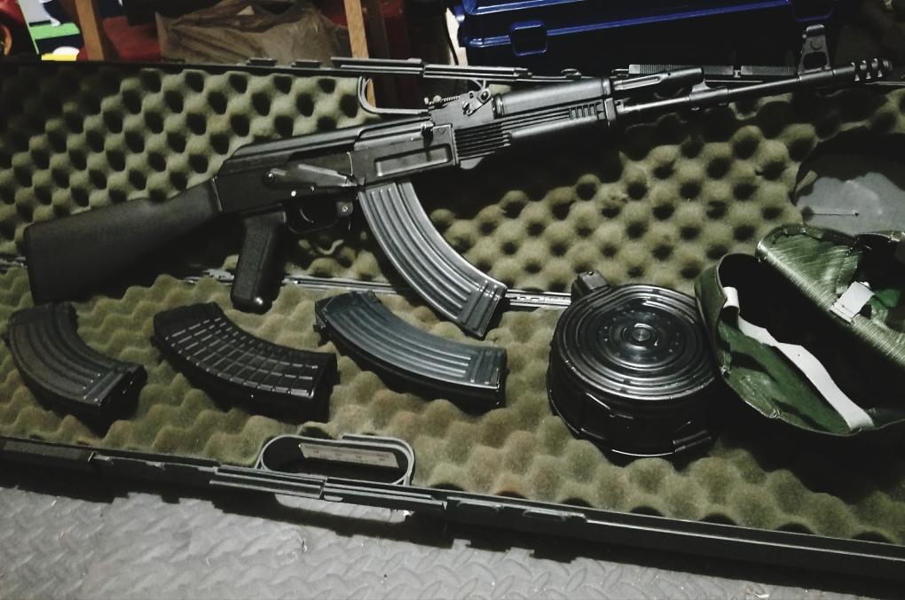 A black AK-style rifle with several magazines and a drum magazine resting in a foam-lined hard case.