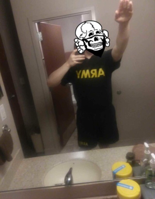 A mirror selfie of an individual in a black U.S. Army t-shirt and shorts performing a Nazi salute, with their face obscured by a white skull mask graphic.
