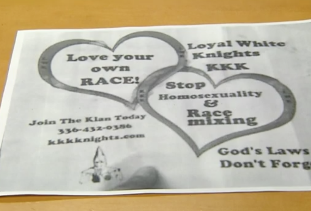 A photograph of a KKK recruitment flyer from the Loyal White Knights featuring interlocking hearts with racist and homophobic text, a phone number, and a website address.