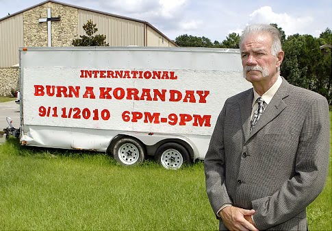 A man with grey hair and a mustache wearing a suit stands in front of a white trailer with red text advertising 'International Burn a Koran Day' on September 11, 2010.