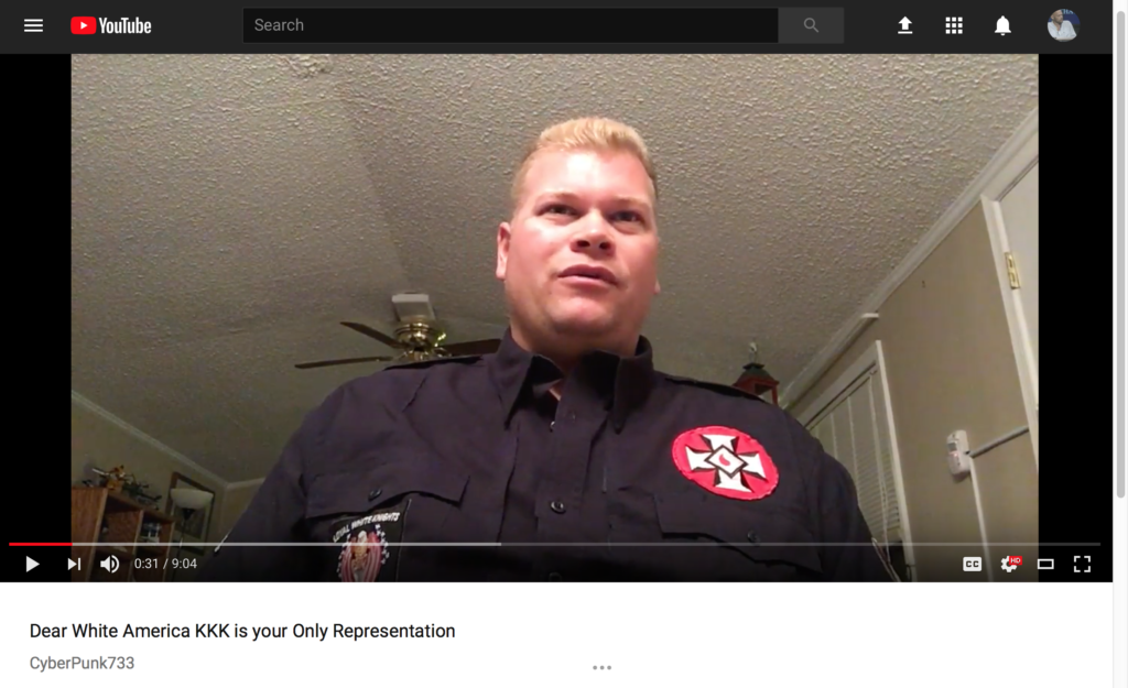 A screenshot of a YouTube video titled 'Dear White America KKK is your Only Representation' featuring a Caucasian man with blonde hair wearing a black shirt with a KKK patch.