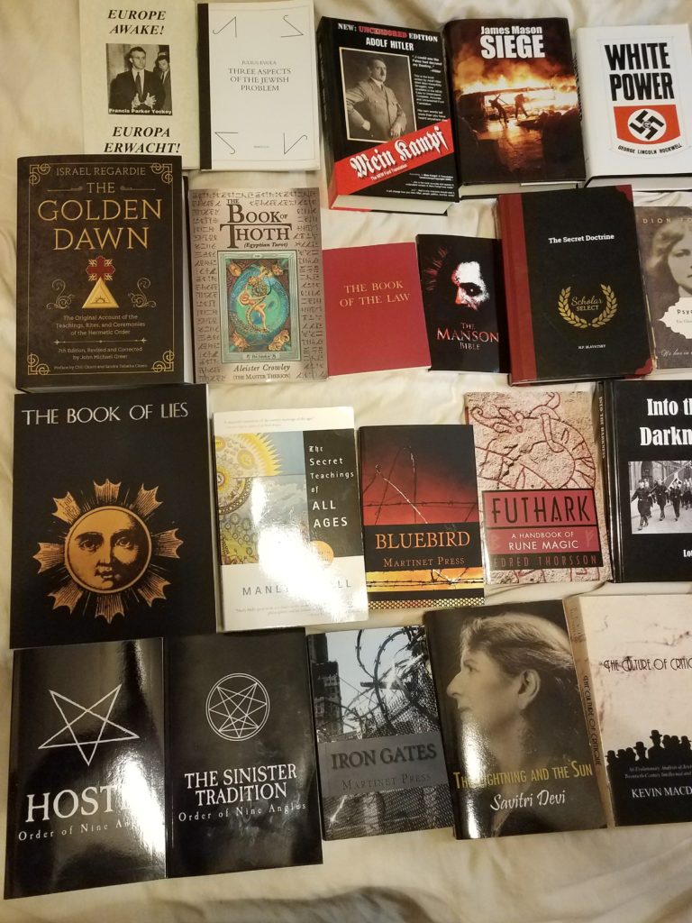 A collection of books related to white supremacy, Neo-Nazism, and occultism, including titles like Mein Kampf, Siege, and White Power, laid out on a light-colored surface.