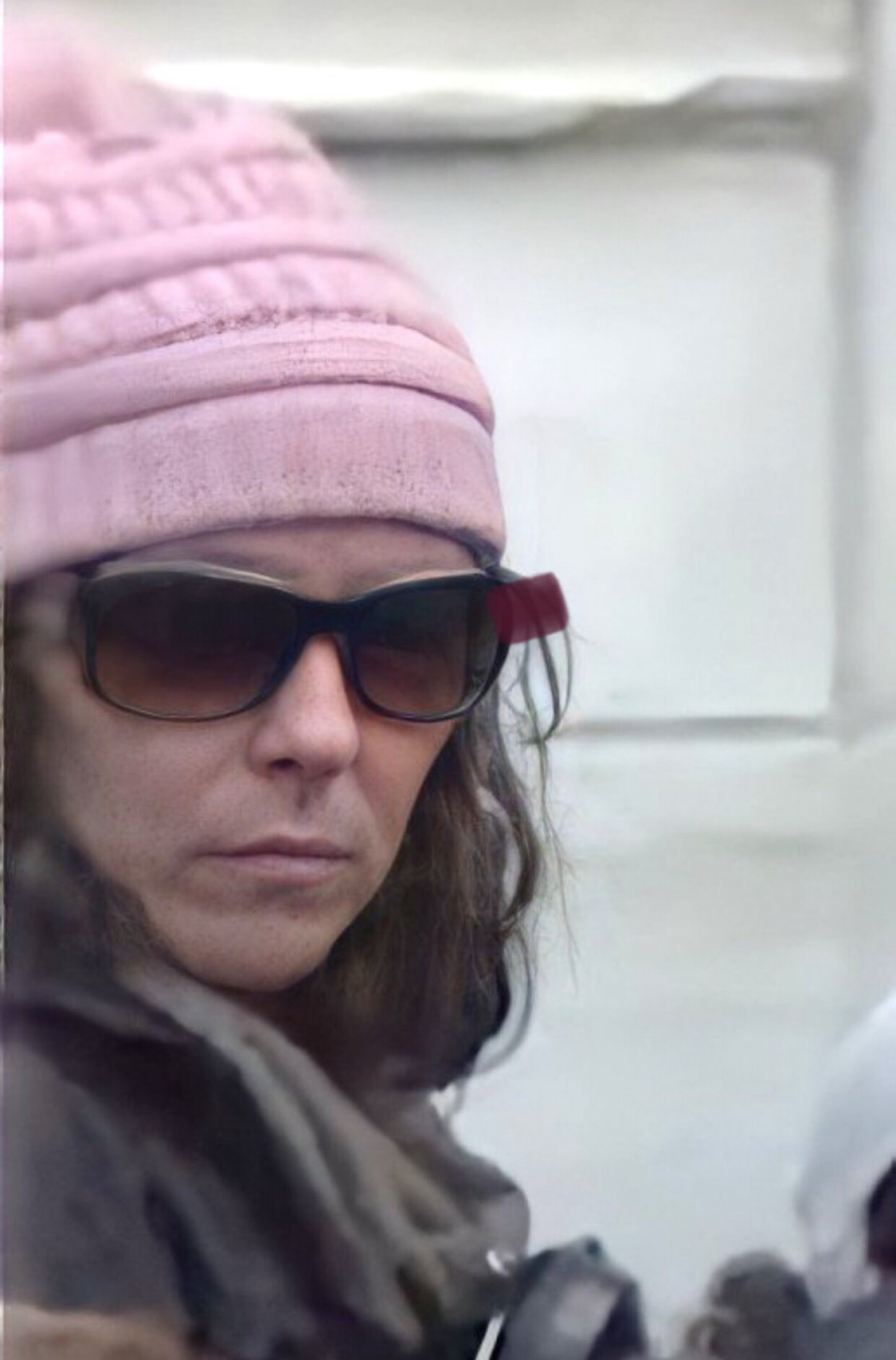 A close-up photograph of a woman wearing a pink knit hat and dark sunglasses, identified in the context as the 'Pink Hat Lady' from the January 6th Capitol attack.