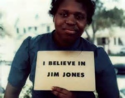 A photograph of a Black woman holding a sign that reads 'I BELIEVE IN JIM JONES'.