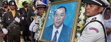 Cambodian military personnel in uniform carrying a large framed portrait of an Asian man during a formal procession.