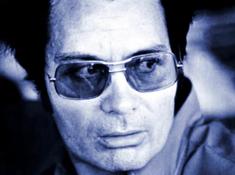 A close-up, blue-tinted photograph of Jim Jones wearing large aviator glasses and having dark hair.