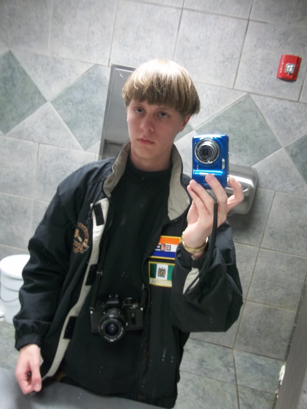 Photo selfie taken by Roof in public restroom. Note him holding one camera and another hanging from strap around his neck