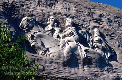 A photograph of the Stone Mountain Confederate Memorial carving in Georgia, depicting Jefferson Davis, Robert E. Lee, and Thomas 'Stonewall' Jackson on horseback against a granite rock face.