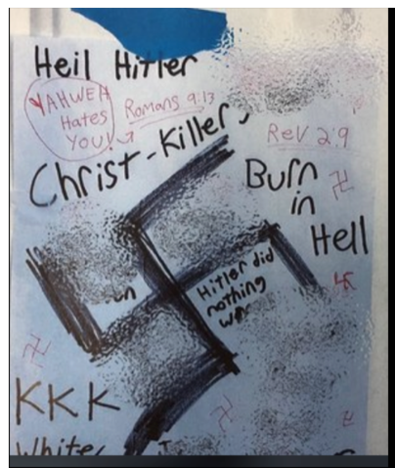 A photograph of a handwritten document containing white supremacist and antisemitic hate speech. The document features a large, crudely drawn swastika in the center, surrounded by text such as 'Heil Hitler', 'Christ-Killer', 'Burn in Hell', 'KKK', 'YAHWEH Hates YOU!', 'Hitler did nothing wrong', and biblical references like 'Romans 9:13' and 'Rev 2:9'. Several smaller swastikas are also drawn on the page.